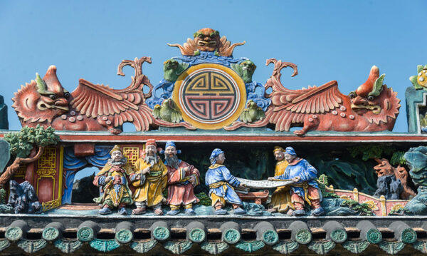 Detail of a tiled rooftop with various colorful carvings, including miniature human figures in classical garb, mythical animals, bridges, trees, buildings, and ornamental rocks.