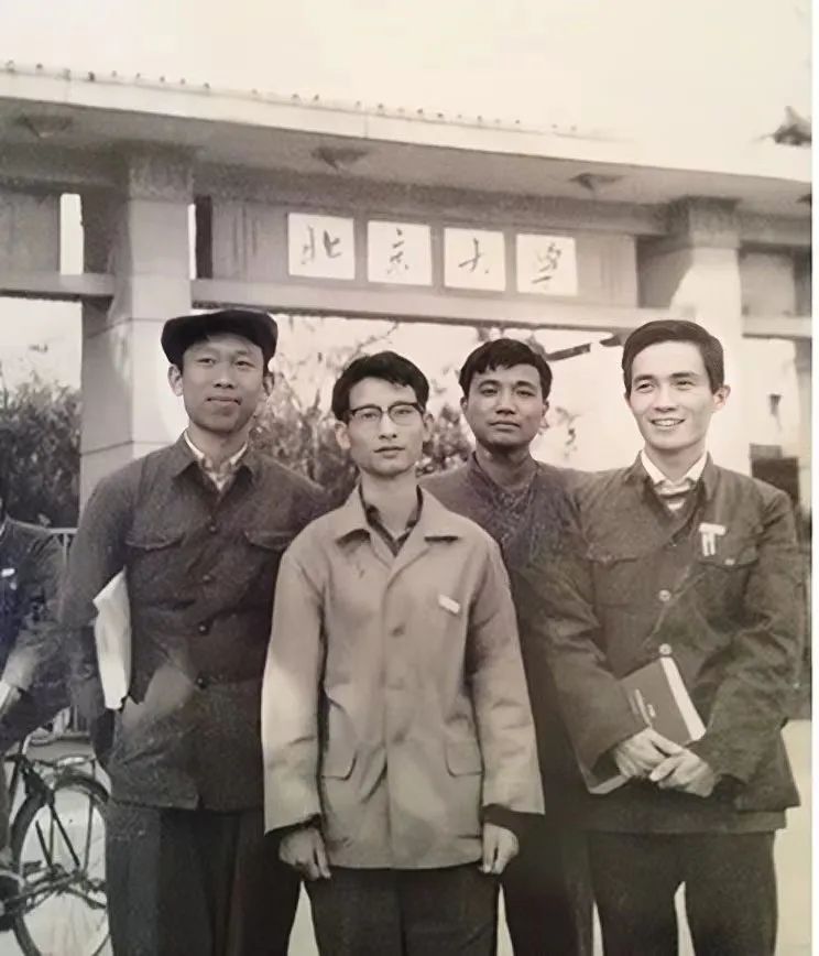 A sepia-tinted photo of four young men, holding books and dressed in humble workers clothing, standing in front of the gate of Peking University.
